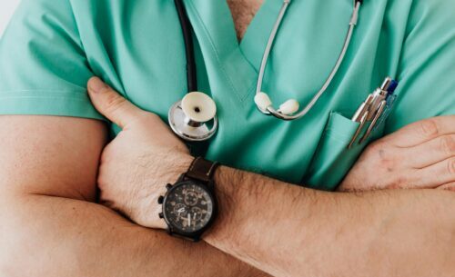 Close-up of a healthcare professional with arms crossed wearing medical scrubs and stethoscope.