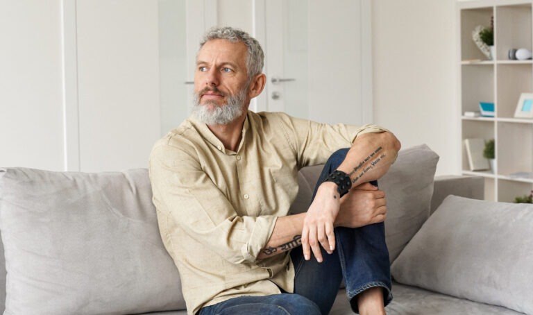 Relaxed mature thoughtful man relaxing sitting on sofa and thinking at home